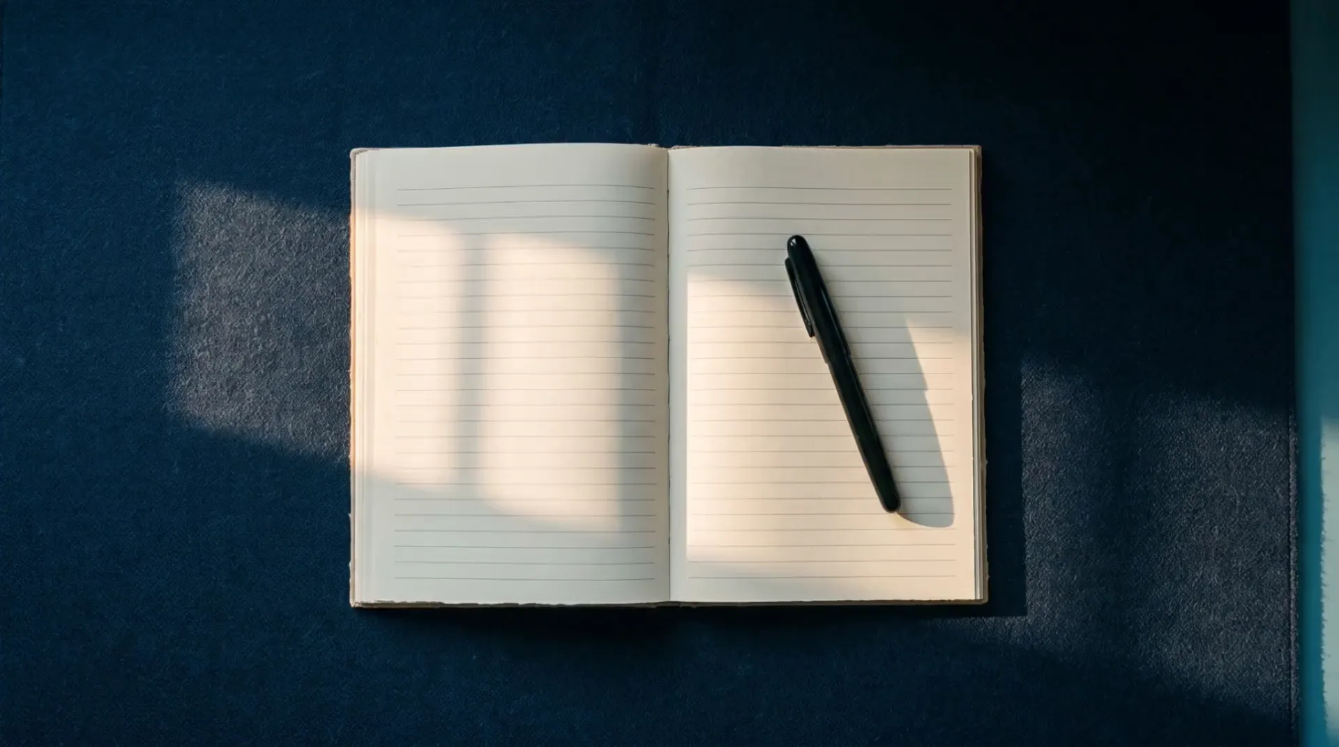 Illustrative open ruled journal and capped fountain pen on a navy wool desk pad